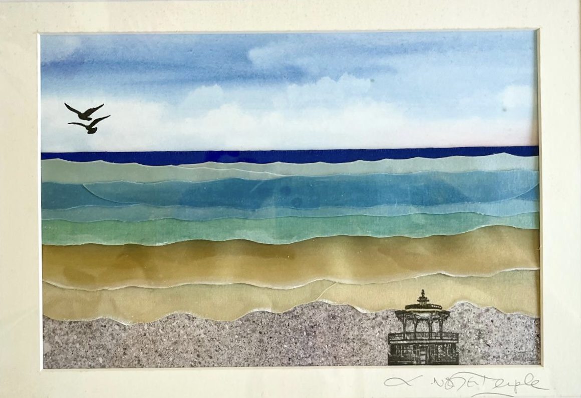 The image is a mixed media artwork titled Bandstand Blues, depicting a serene seascape. The scene is composed of layered, cut paper or translucent materials in soft gradients to represent the sea, sand, and sky. The sky transitions from light blue near the horizon to a deeper blue at the top, with soft white clouds. The sea is illustrated in gently undulating bands of turquoise, blue, and green, mimicking the movement of waves. Two black silhouettes of birds fly over the water in the distance, adding a sense of calm and motion. The foreground features layers of sandy tones leading to a speckled, grey shoreline. In the lower right corner, there is a fine black line drawing of a Victorian-style bandstand, adding a touch of architectural detail and nostalgia to the natural scene. The combination of collage and illustration creates a harmonious and peaceful coastal composition.